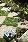 Chequered pattern of stone slabs and squares of lawn in sunny garden with flower bed to one side