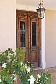 Rose bush and lantern outside antique, Indian front door with glass panels and metal grille