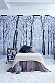 Französisches Bett mit gestrickter Tagesdecke und Kissen auf Kunstschnee bedecktem Boden vor Poster mit Winterlandschaft