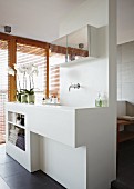 White partition element with sink, surface and shelves in front of glass wall with wooden louver blinds