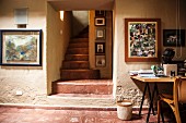 Arbeitsraum mit schmalem Treppenaufgang und Fotosammlung über dem Arbeitstisch an rustikaler Wand