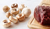 Raw Beef Tenderloin on a Wooden Cutting Board with Raw Mushrooms