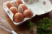 Frische Eier im Eierkarton neben Petersilie und Schneebesen