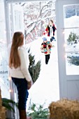 Mädchen in Tür stehend empfängt durch Schnee laufende Gäste