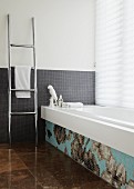 Badezimmer mit grauen Mosaikfliesen an der Wand und eine mit einem Blumenmosaik dekorierte Badewanne
