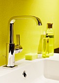Glänzende Waschbeckenarmatur vor gelber Badezimmerwand