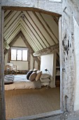 Comfortable double bed on floor below steep, exposed roof structure of half-timbered house