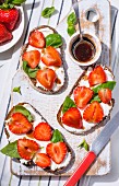 Slices of bread topped with cream cheese, strawberries, balsamic vinegar and basil