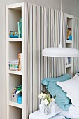 Pendant lamp with white lampshade in front of shelving units with striped fabric covers used as headboard