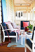 White wooden bench and armchairs with dark blue cushions around table on veranda with white balustrade and turned columns