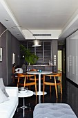 Narrow, masculine seating area with dark grey wall and designer furniture next to white, fitted cupboards