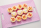 Cupcakes with icing spelling out 'Merry Xmas', on a tray