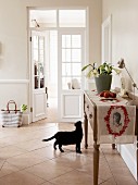 Flower arrangement and runner on sideboard in pale country-house kitchen with black cat on tiled floor