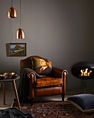 Cushion printed with portrait of man on leather armchair, copper lampshades and modern fireplace