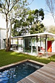 View across wooden terrace and pool to living area behind glass facade