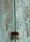Verwitterte Holztür mit abgeblätterter blauer Farbe und Vorhängeschloss (Ausschnitt)