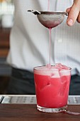 Einen pinkfarbenen Cocktail durch ein Sieb gießen