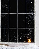 Candle burning in snow covered house window