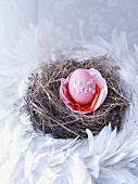 Dyed egg decorated with alphabet noodles in nest of hay and feathers