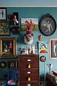 Hotchpotch of framed pictures and flea market finds on turquoise living room wall