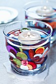 Colourful buttons as decoration in water-filled candle lantern with floating candle