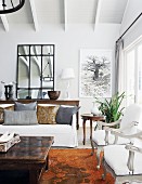 Pale, elegant living room with white, antique, upholstered armchairs and rustic coffee table in country-house ambiance