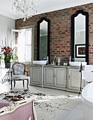 Two tall mirrors above vintage washstand cabinet against brick wall in shabby chic bathroom