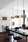 Modern dining room with black dining table below designer pendant lamps; black wood-burning stove in background next to basket of firewood