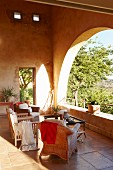 Various armchairs and coffee table on stone-flagged loggia floor and view of sunny garden through rounded arches