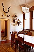 Carved chairs in dining area with ceiling lamp and animal trophies on wall above doorway