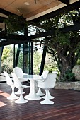Sitzplatz mit weissen Schalenstühlen im Bauhausstil auf Holzterrasse und Blick in Garten