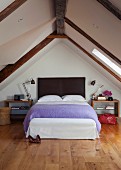Modern attic bedroom with light wooden floor and comfortable double bed below gabled ceiling