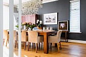 Elegant dining room with anthracite walls, long dining table and upholstered armchairs; pretty sea glass chandelier above table