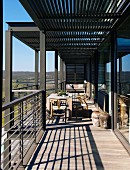 Sonniger Balkon mit Metallstützen, Metallgeländer und herrlichem Weitblick; in der Mitte ein einfacher Holztisch mit Stühlen und afrikanischen Bodenvasen