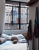 Doppelbett in Schlafzimmer mit Industriefenster und mit Blick auf Feuertreppe und Fensterfronten des Nachbargebäudes