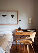50s wooden chair at delicate writing desk against wall and framed drawings above bed