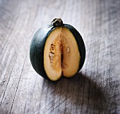 A green squash, sliced to show the centre, on a wooden surface