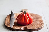 A beef tomato with a knife on a chopping board