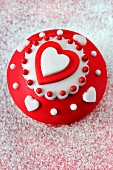 A cupcake with red and white icing and hearts