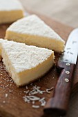 Cheesecake with grated coconut, partly sliced, on a chopping board
