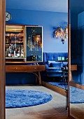 50er Jahre Barschrank mit Spiegeltüren und vergoldete Leuchter aus den 70ern über blauem Samtsofa in Wohnzimmer mit blauen Wänden