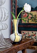 White ranunculus in small 60s vase; traditional cabinet in peasant painting style in background