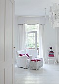 Bedroom entirely in white - armchair with white loose cover and white-painted wicker trunk on white wooden floor in front of white, floor-length curtains