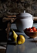 Birnen neben Schale mit Tomaten und weisser Vintage Emaille Behälter mit Deckel auf Holztisch