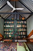 Schlafbereich vor Bücherregalen an Giebelwand unter Satteldach mit Metallabdeckung