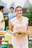 Woman holding tray of barbecued food & salad