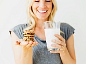 A woman holding a stack of biscuits in one hand and a glass of milk in the other