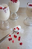 Joghurt mit Granatapfelkernen in drei Gläsern und auf Löffel