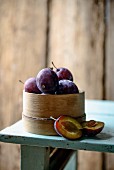 Plums in a woodchip basket on a wooden table