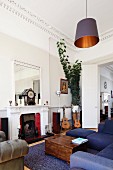 Partially visible lounge furniture and old wooden trunk in front of open fireplace and guitar on stand in corner of grand interior; pendant lamp with black and golden lampshade in foreground